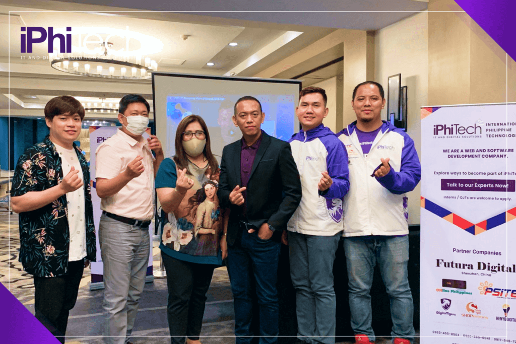 company representatives doing a finger hearts with potential clients and partners in a hotel lobby with marketing material of the company iPhiTech IT and Digital Solutions